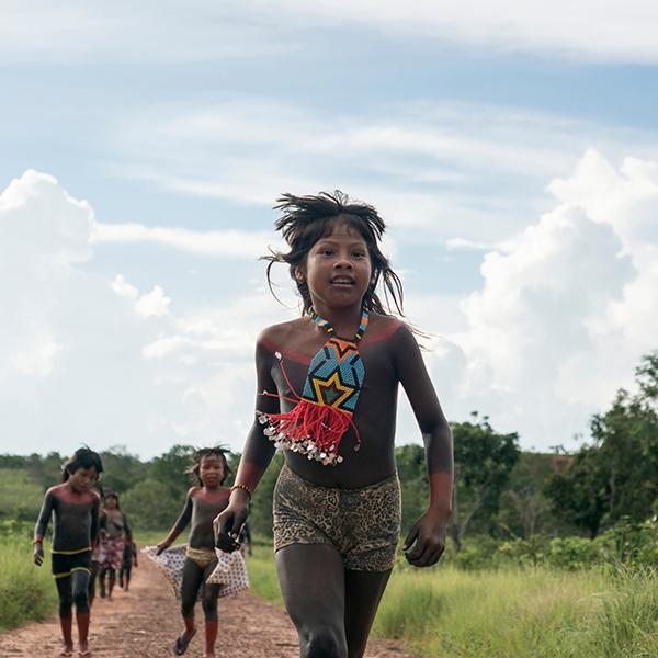 indigenous children in Brasil, running down dirt road with clear blue sky behind